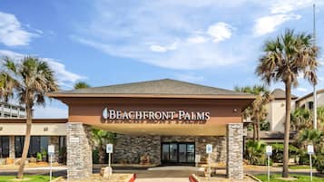 The entrance of a hotel named Beachfront Palms with a stone facade and palm trees.