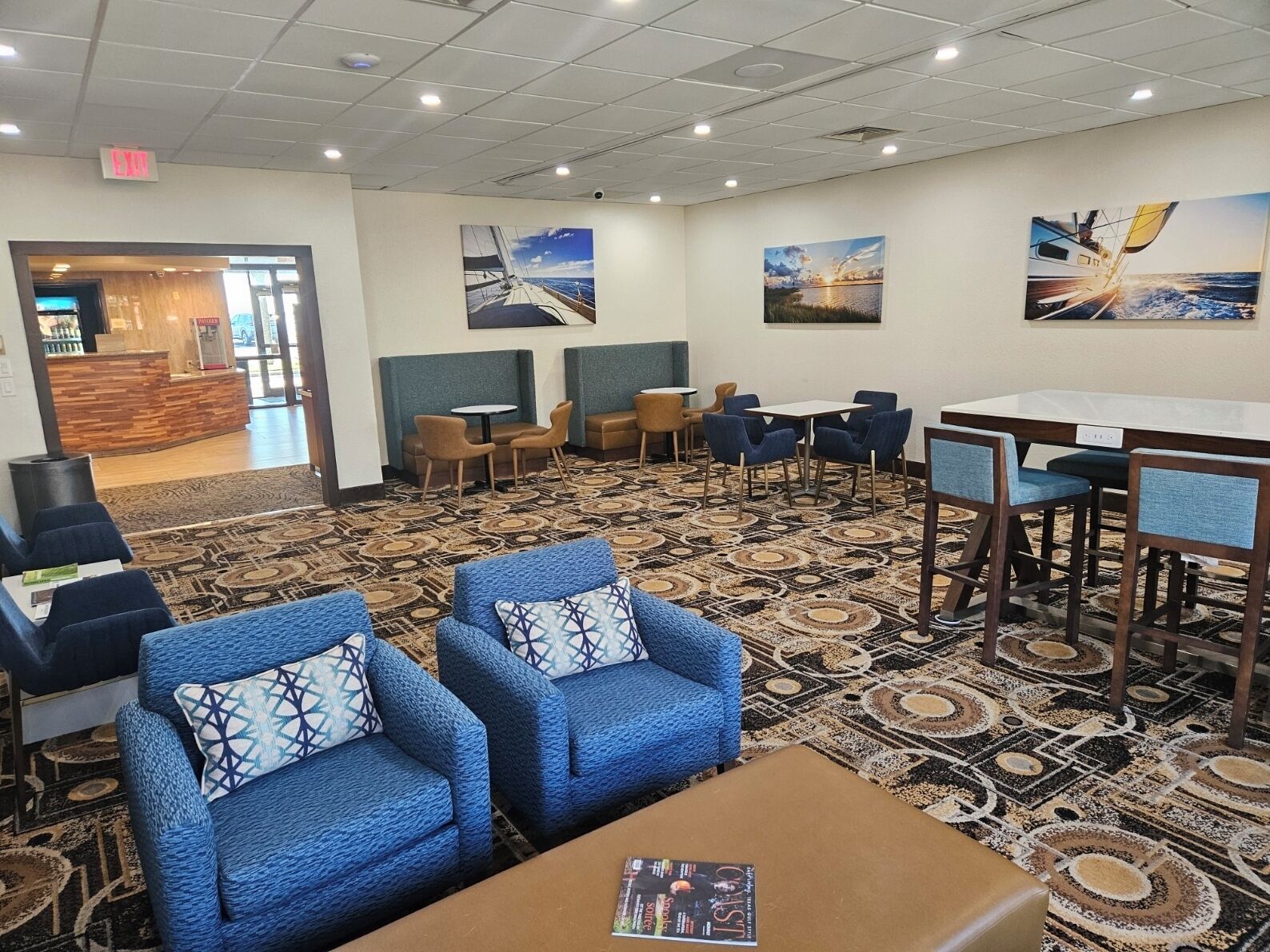 A hotel lobby with blue armchairs, a reception desk, and artwork on the walls.