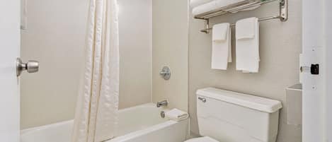 A bathroom with a bathtub, toilet, and a towel rack with folded towels.