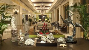 A spacious hotel lobby with a chandelier, seating area, and decorative elements like vases and sculptures.