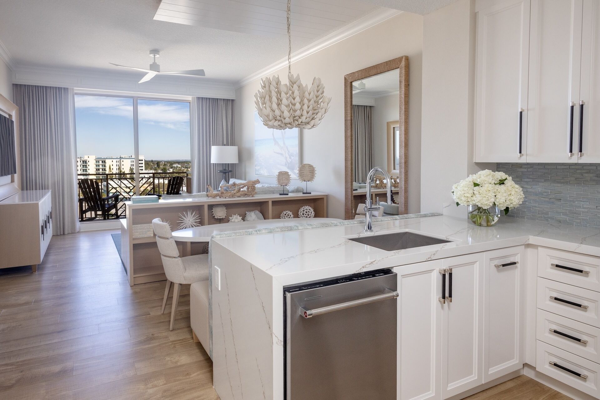 A modern kitchen with a central island, a dining area with chairs, a large window with a view, and a ceiling fan.