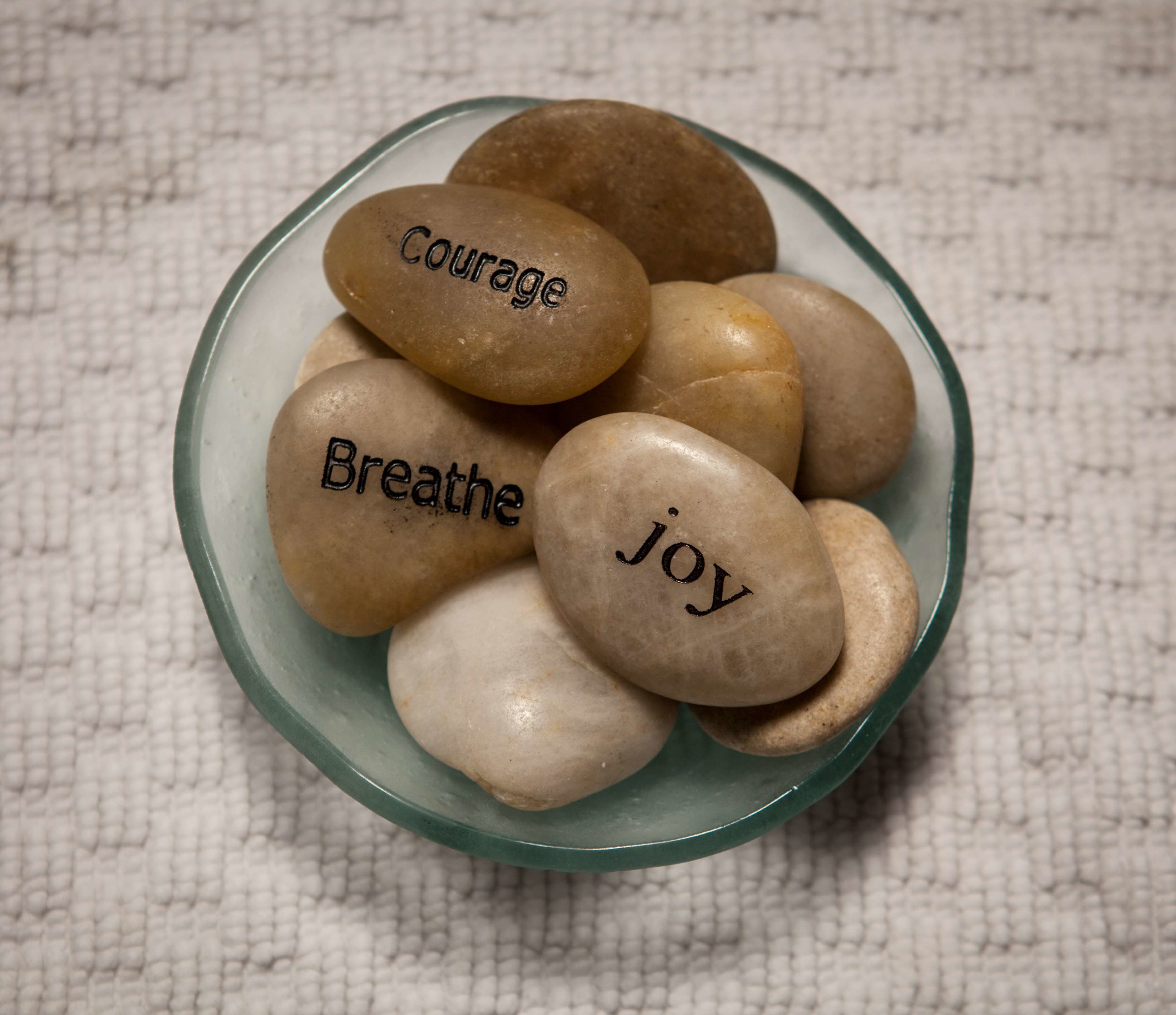 A bowl of smooth, oval stones with words like "Courage," "Breathe," and "Joy" engraved on them.