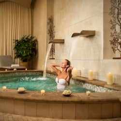 Guests can unwind in a serene spa setting with a hot tub, candles, and lush greenery.