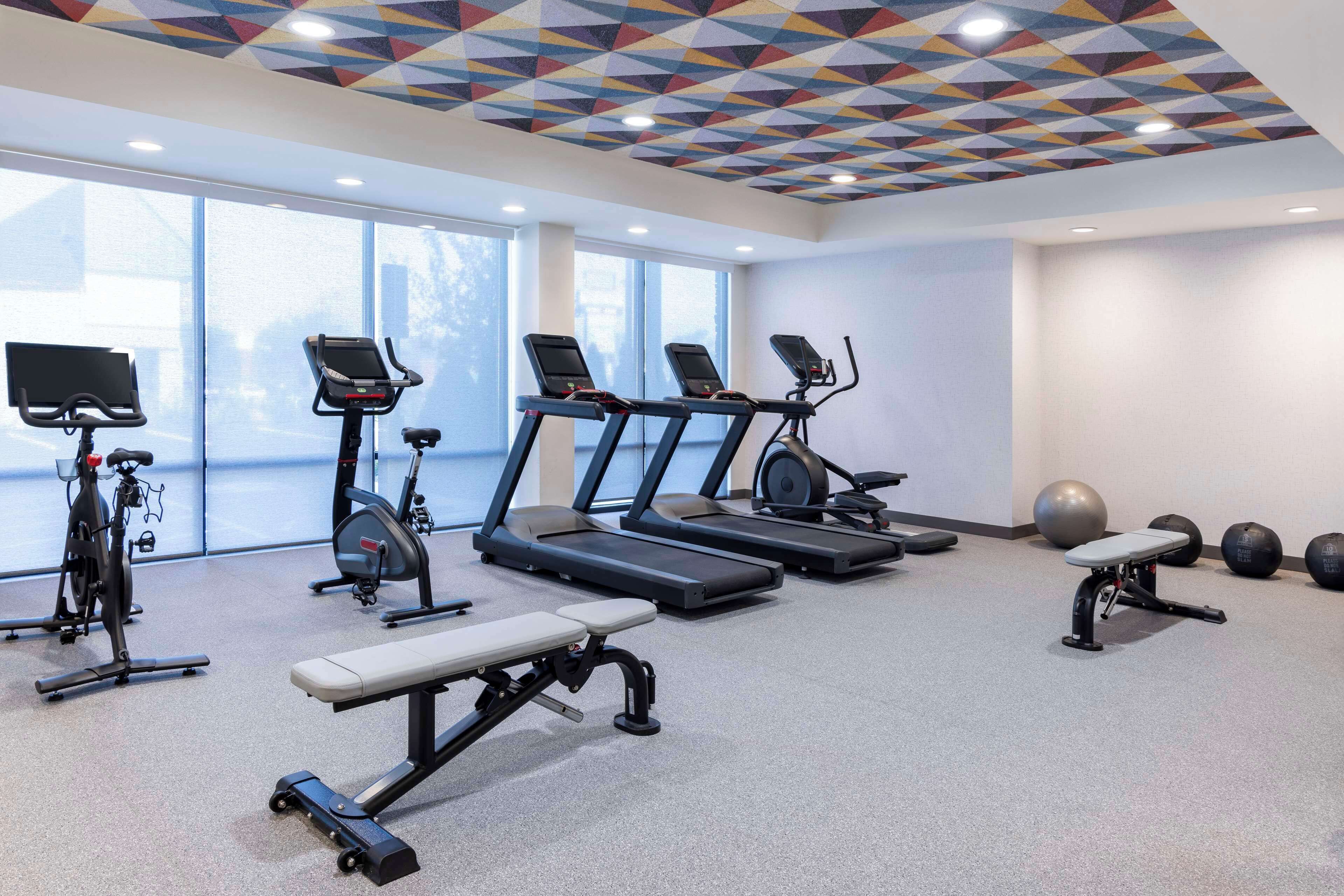 Un gimnasio con cintas de correr, bicicletas estáticas, una banca y pelotas de ejercicio.