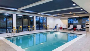 Una piscina interior con paredes de vidrio transparente, sillas amarillas y un diseño moderno de techo.