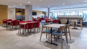 Un comedor moderno con sillas rojas y azules, mesas y un amplio ventanal con vistas.