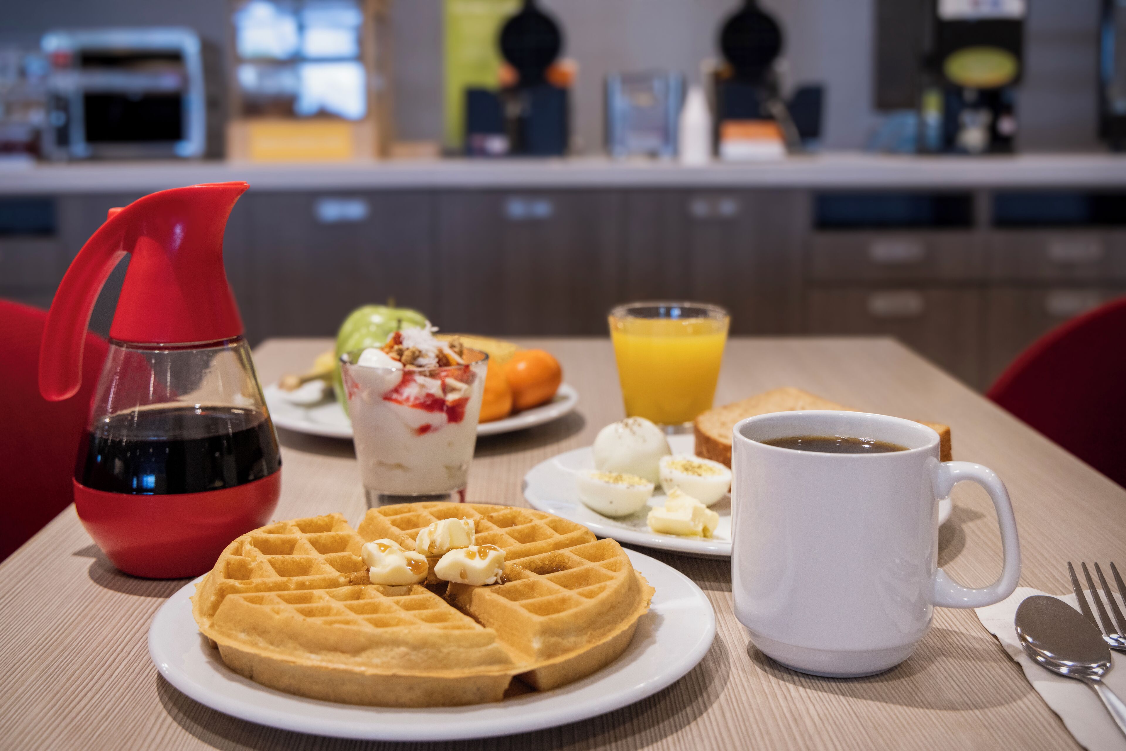 En morgenmadsopstilling med en vaffel, æg, ristet brød og en kop kaffe på et bord.