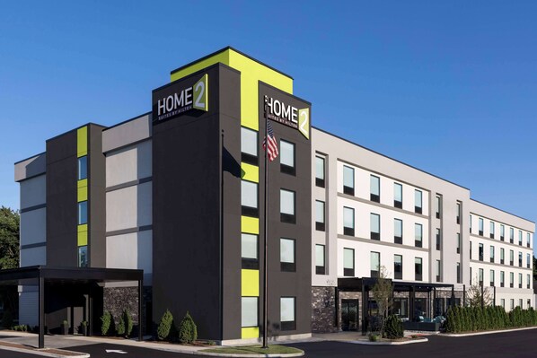 A modern hotel building with a prominent 'HOME 2' sign, featuring a two-story structure with a flat roof and a mix of window sizes. - Home2 Suites by Hilton East Haven New Haven (East Haven)