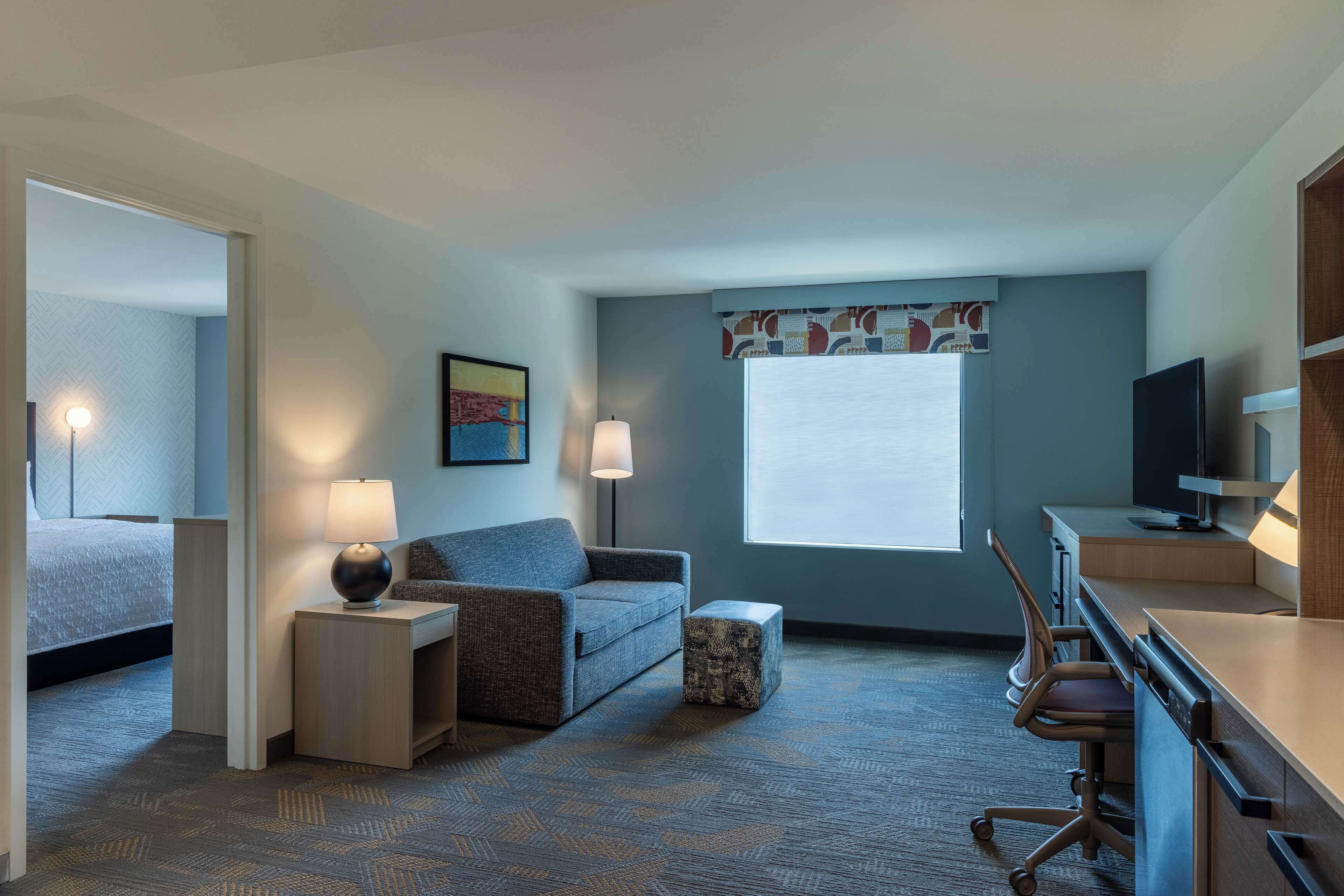 Habitación de hotel con cama, sofá, escritorio, silla y televisor.
