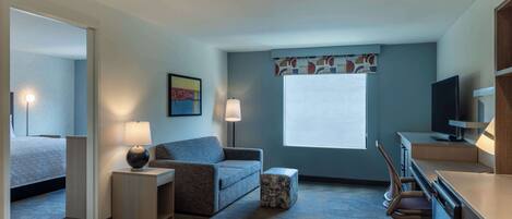 Habitación de hotel con cama, sofá, escritorio, silla y televisor.