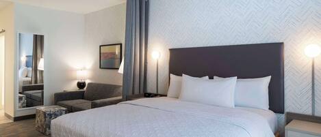 A hotel room with a large bed, a sofa, a small table, a lamp, and a mirror.