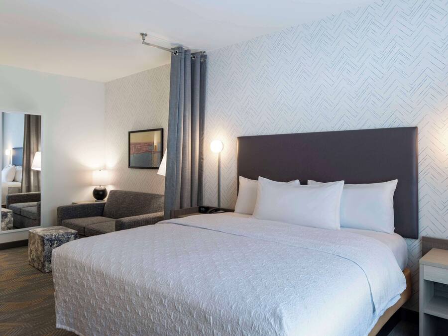 Camera d'albergo con un grande letto, un divano, un tavolino, una lampada e uno specchio.