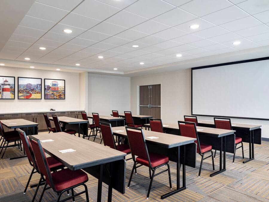 A conference room with multiple tables and chairs, a projector screen, and framed pictures on the wall.