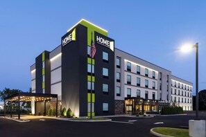 A modern hotel with a prominent 'HOME' sign, a covered entrance, and a well-lit facade. - Home2 Suites by Hilton East Haven New Haven (East Haven)