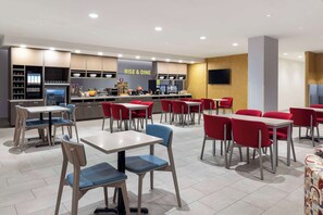 A modern restaurant with multiple dining tables and chairs, a kitchen area, and a 'RISE & DINE' sign. - Home2 Suites by Hilton East Haven New Haven (East Haven)
