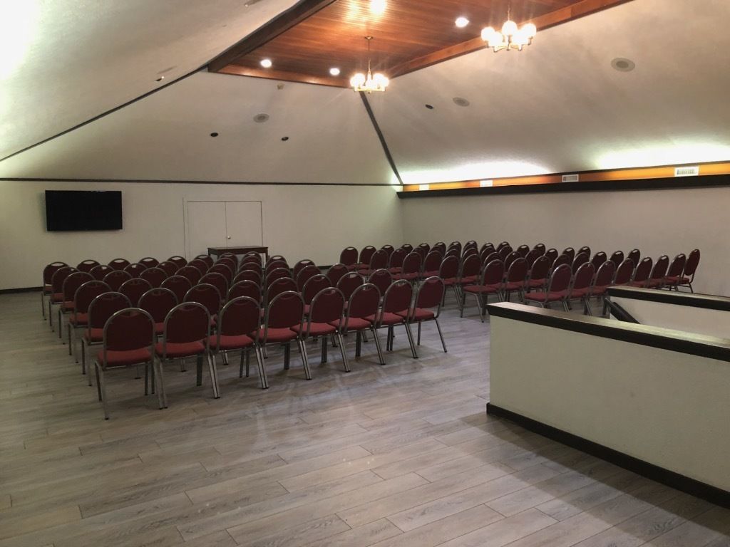 Un salón de conferencias con filas de sillas rojas, techo de madera y una televisión de pantalla plana en la pared.