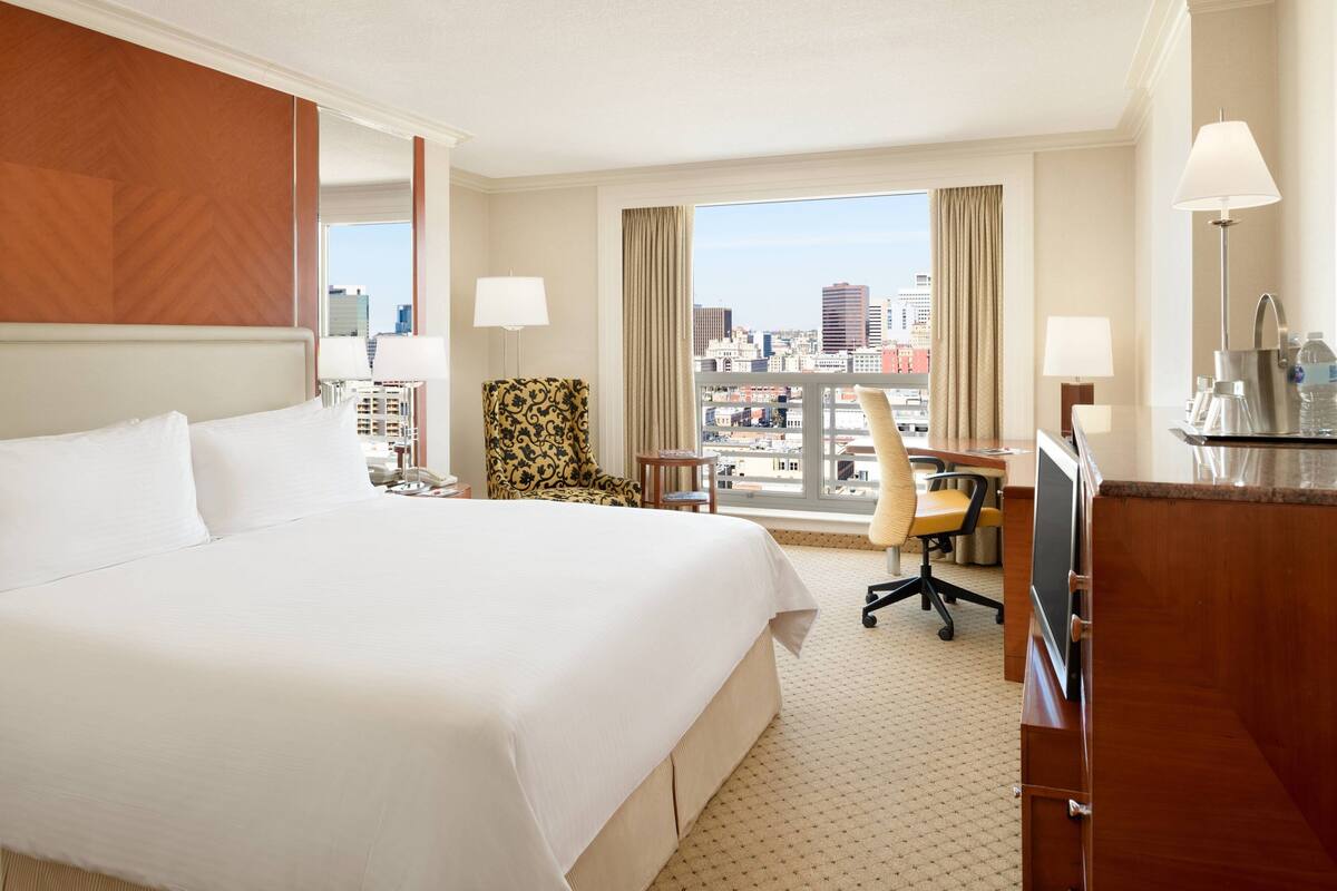 Une chambre d’hôtel avec un grand lit, un bureau avec une chaise, un canapé et une vue sur la ville.
