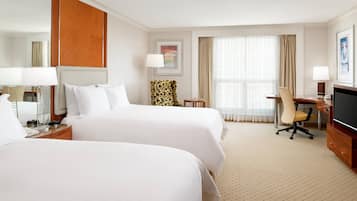 A hotel room with two beds, a desk, a chair, a TV, and a large window with curtains.