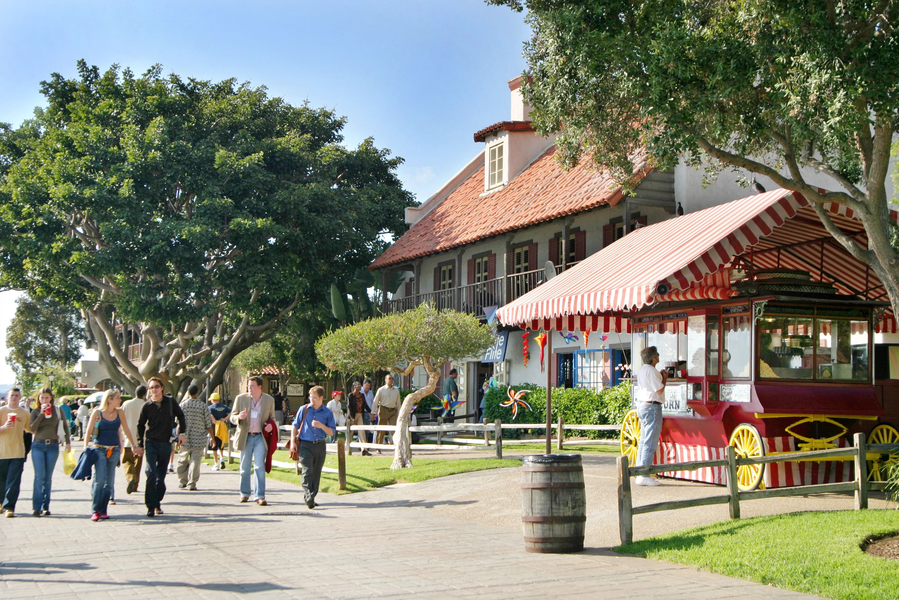 A street with pedestrians, a red and white striped cart, and a building with a red-tiled roof.