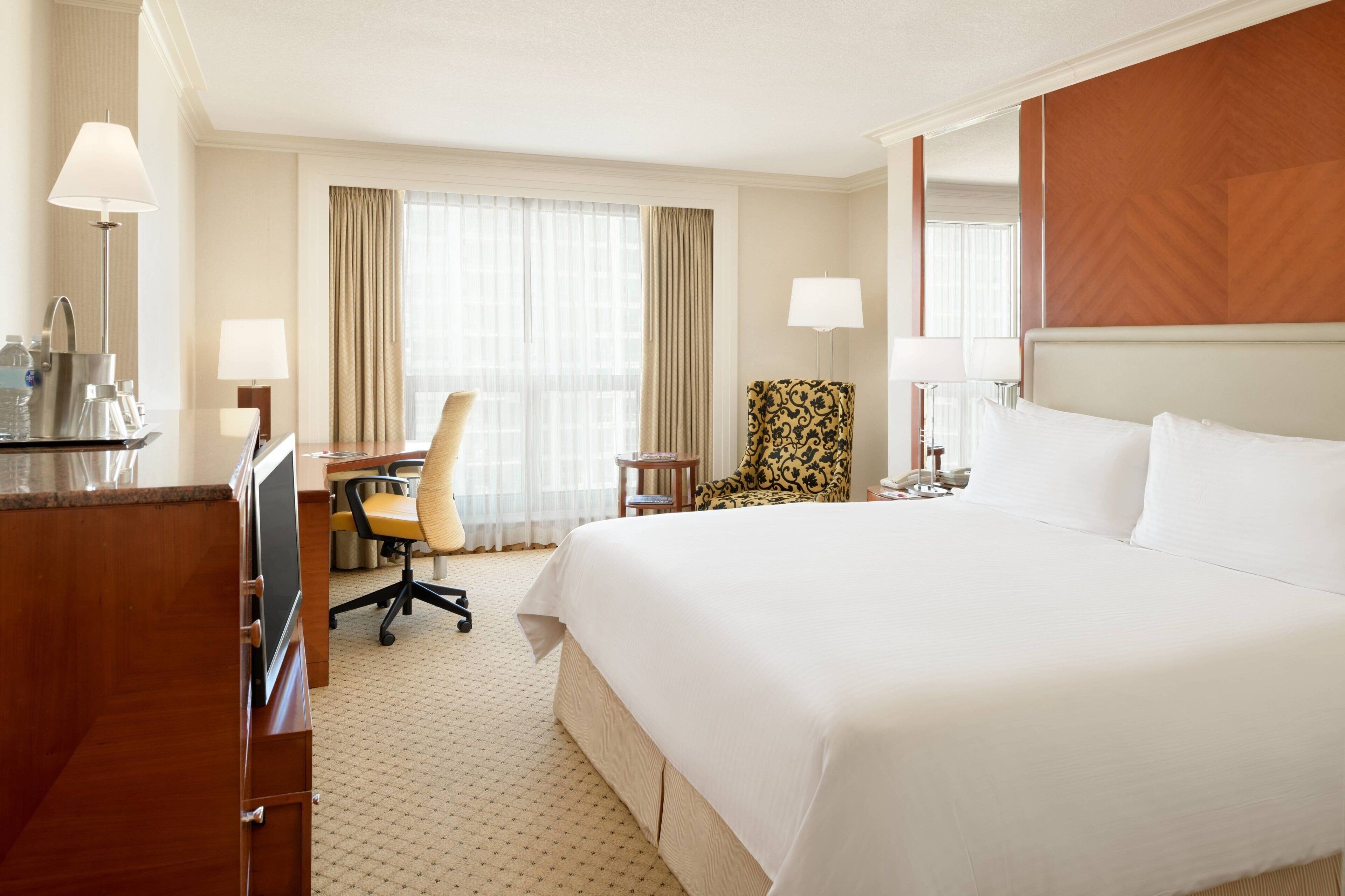 Une chambre d’hôtel avec un grand lit, un bureau avec une chaise, une petite table et une lampe.