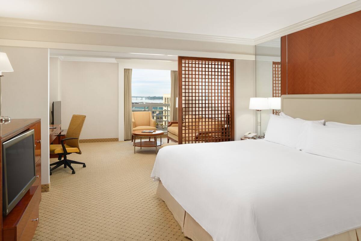 Une chambre d’hôtel avec un grand lit, un bureau avec une chaise, une télévision et une vue sur la ville par la fenêtre.