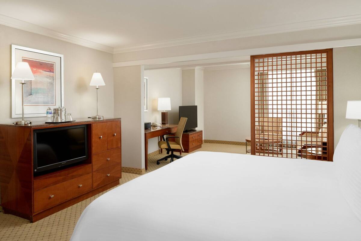 Une chambre d’hôtel avec un grand lit, un bureau équipé d’un ordinateur, une télévision et une cloison en bois.