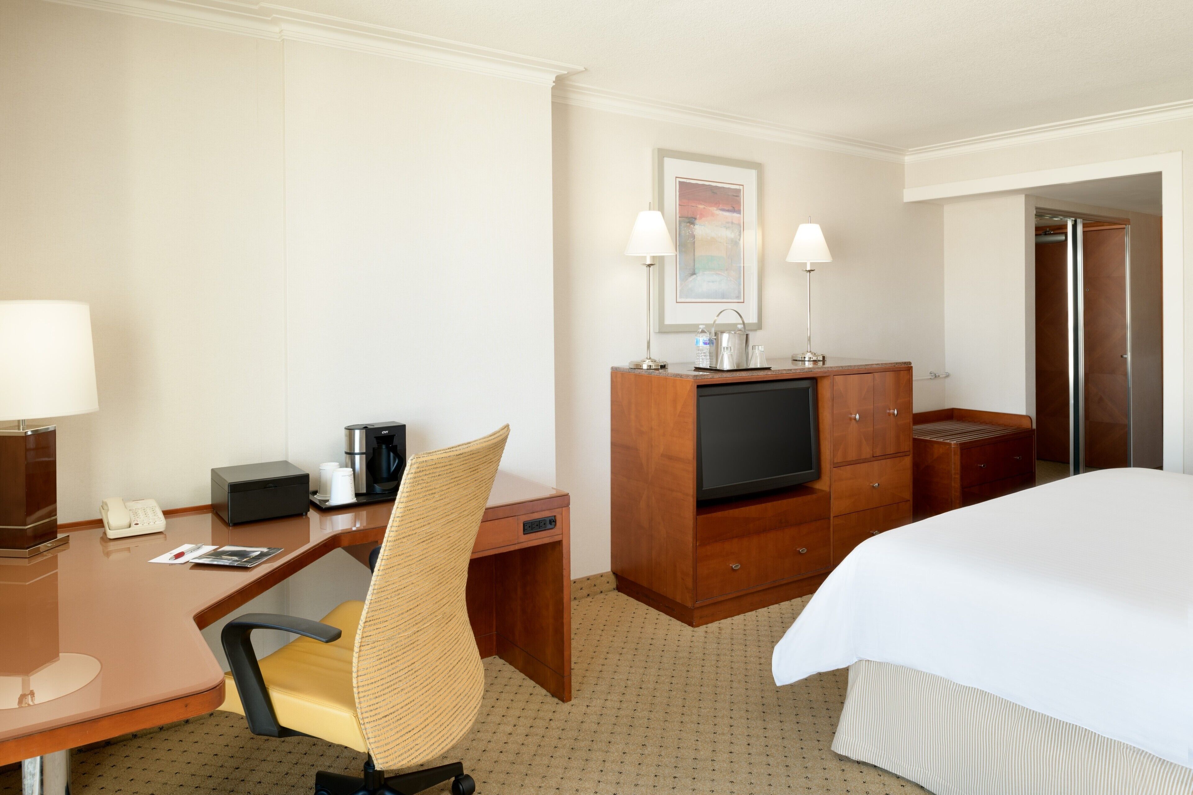 A hotel room with a bed, a desk with a chair, a television, a coffee maker, and a telephone.