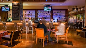A bar area with multiple seating options, a variety of liquor bottles on shelves, and two televisions mounted on the wall.