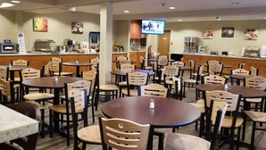 Un restaurant doté de plusieurs tables et chaises, d’une machine à café, d’un écran de télévision et présentant divers produits alimentaires.