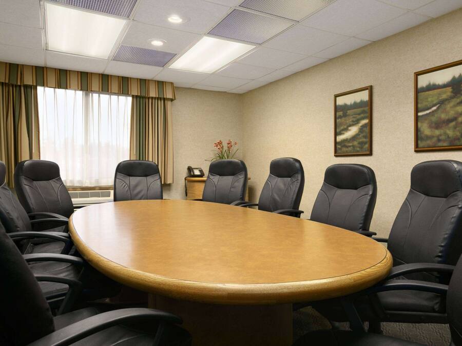 A conference room with a large oval table, black leather chairs, a small side table with a phone, and two framed landscape paintings on the wall.