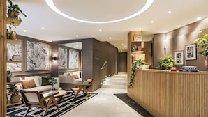 A modern hotel lobby with a reception desk, seating area, and a staircase leading to the upper floors. - Hôtel Maison Pigalle (Paris)