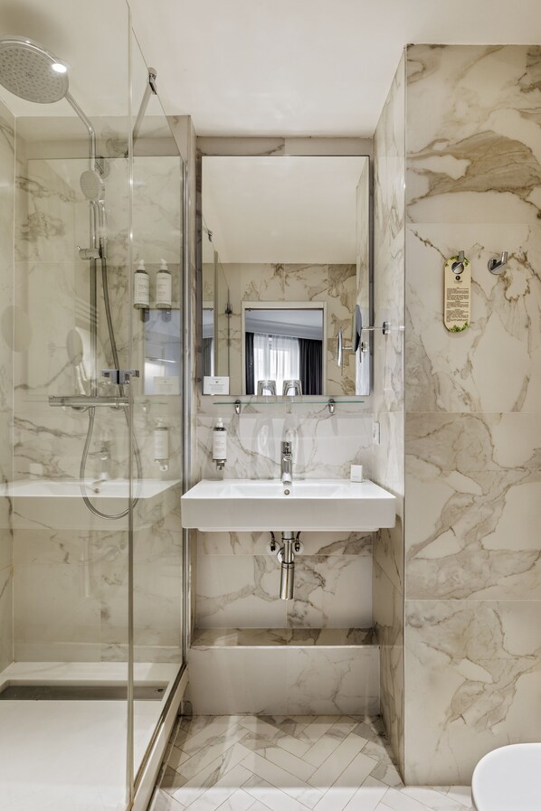 A modern bathroom with a glass-enclosed shower, a marble-tiled sink, and a large mirror.