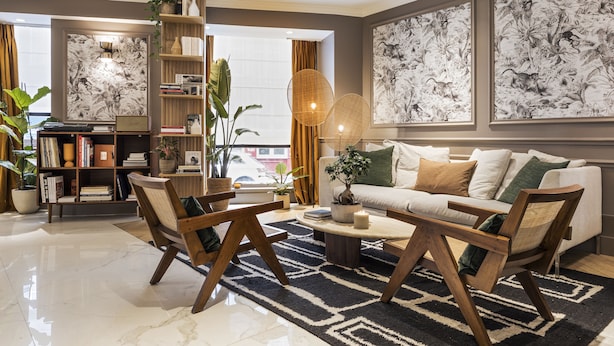 A modern living room with a sofa, coffee table, and chairs. There is a bookshelf with books and decorative items, and a large window with curtains. - Hôtel Maison Pigalle (Paris)