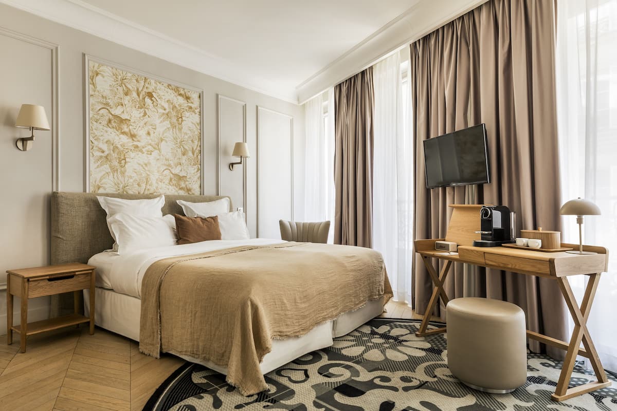 A hotel room with a bed, bedside tables, a desk with a chair, a television, and a coffee maker.