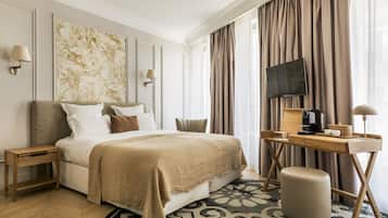 A hotel room with a bed, bedside tables, a desk with a chair, a television, and a coffee maker.