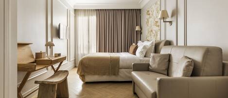 A modern hotel room with a wooden desk, a sofa, a bed, and a large window with curtains.