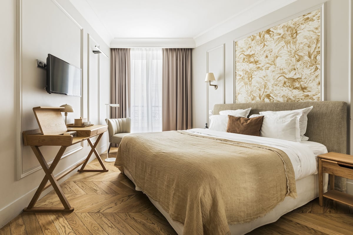 A hotel room with a large bed, a desk with a lamp, a television, and a window with curtains.