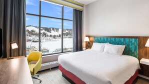 Ein Hotelzimmer mit einem großen Bett, einem Schreibtisch, einem Stuhl und Blick auf eine verschneite Landschaft durch das Fenster.