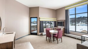 Ein Hotelzimmer mit großem Fenster, einem Essbereich mit Tisch und Stühlen, einem Fernseher und einem Waschbecken.