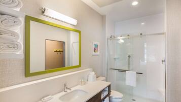 A modern bathroom with a large mirror, a sink, a toilet, and a glass-enclosed shower.