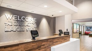 Ein Empfangsschalter mit einem Schild, auf dem 'Welcome to the Great Lakes State' steht, ein digitaler Kiosk und eine 'Hilton Honors'-Plaque.