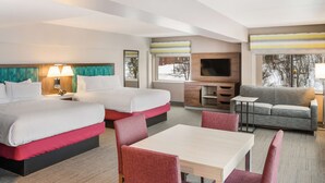 Ein Hotelzimmer mit zwei Betten, einem Schlafsofa, einem Fernseher und einem Essbereich.