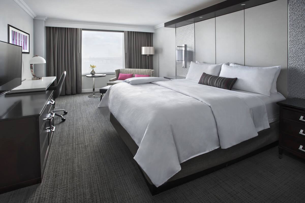 Een moderne hotelkamer met een groot bed, een bureau, een stoel, een tafeltje met een lamp en uitzicht op de stad door het raam.
