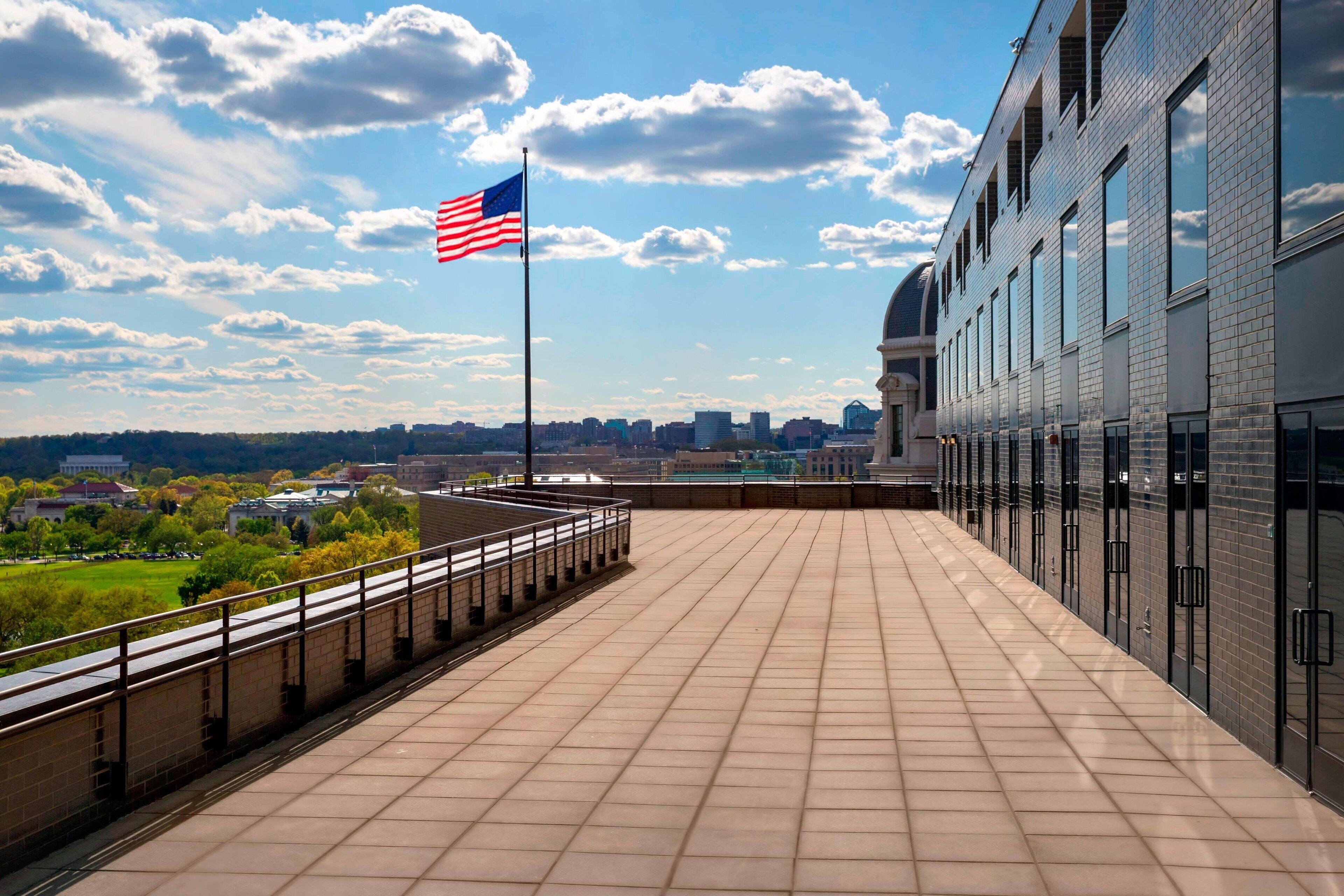 A rooftop terrace with a flag, a cityscape view, and a modern building with large windows.