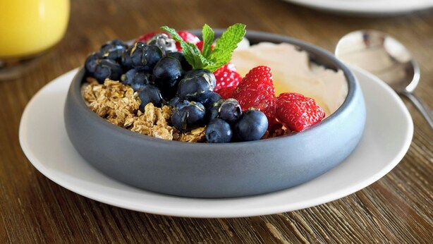 Un tazón de cereal con arándanos, fresas y granola sobre un plato blanco.