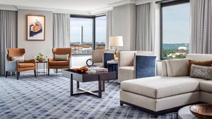 A modern hotel room with a large window offering a city view, a comfortable sofa, a coffee table, and two armchairs. - JW Marriott Washington DC (Washington)