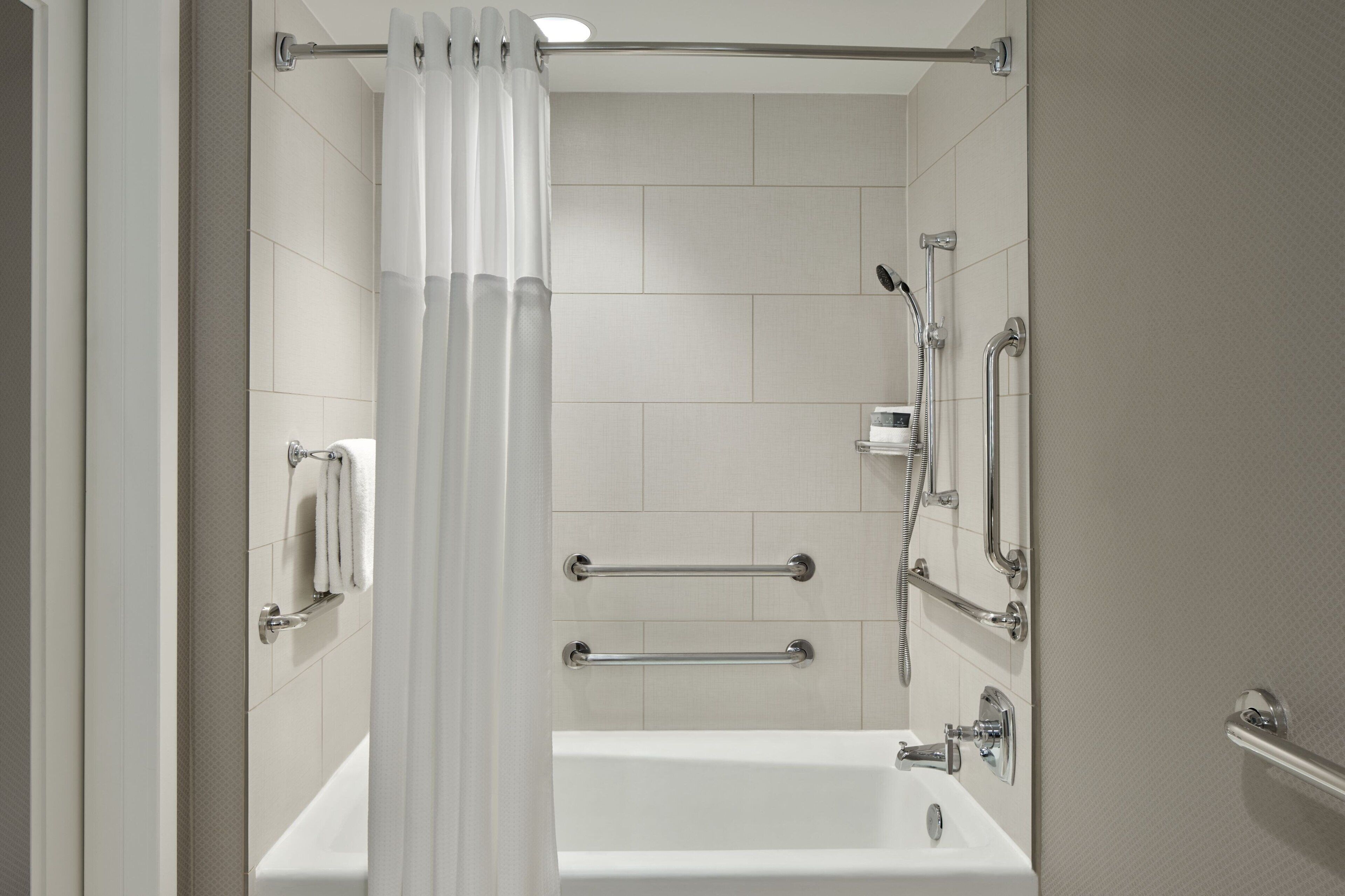 A modern bathroom with a bathtub, grab bars, and a shower control panel.