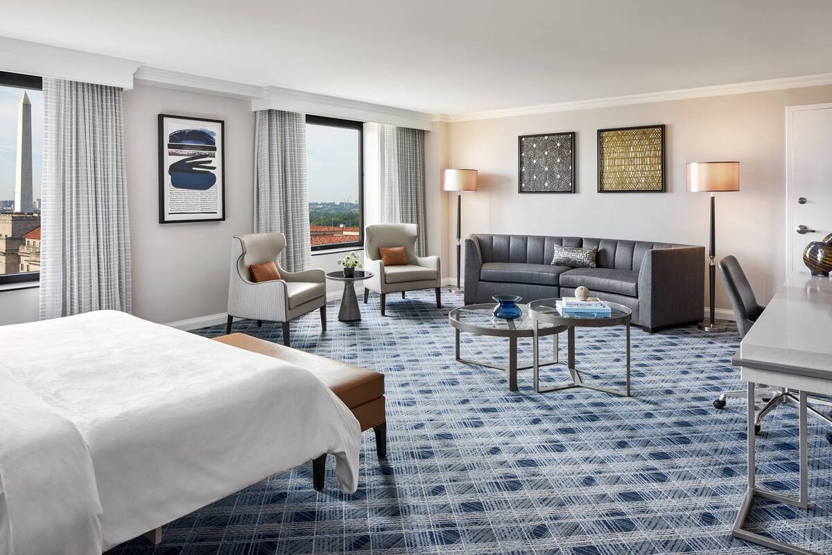 Een hotelkamer met een bed, twee fauteuils, een bank, een salontafel en een bureau.