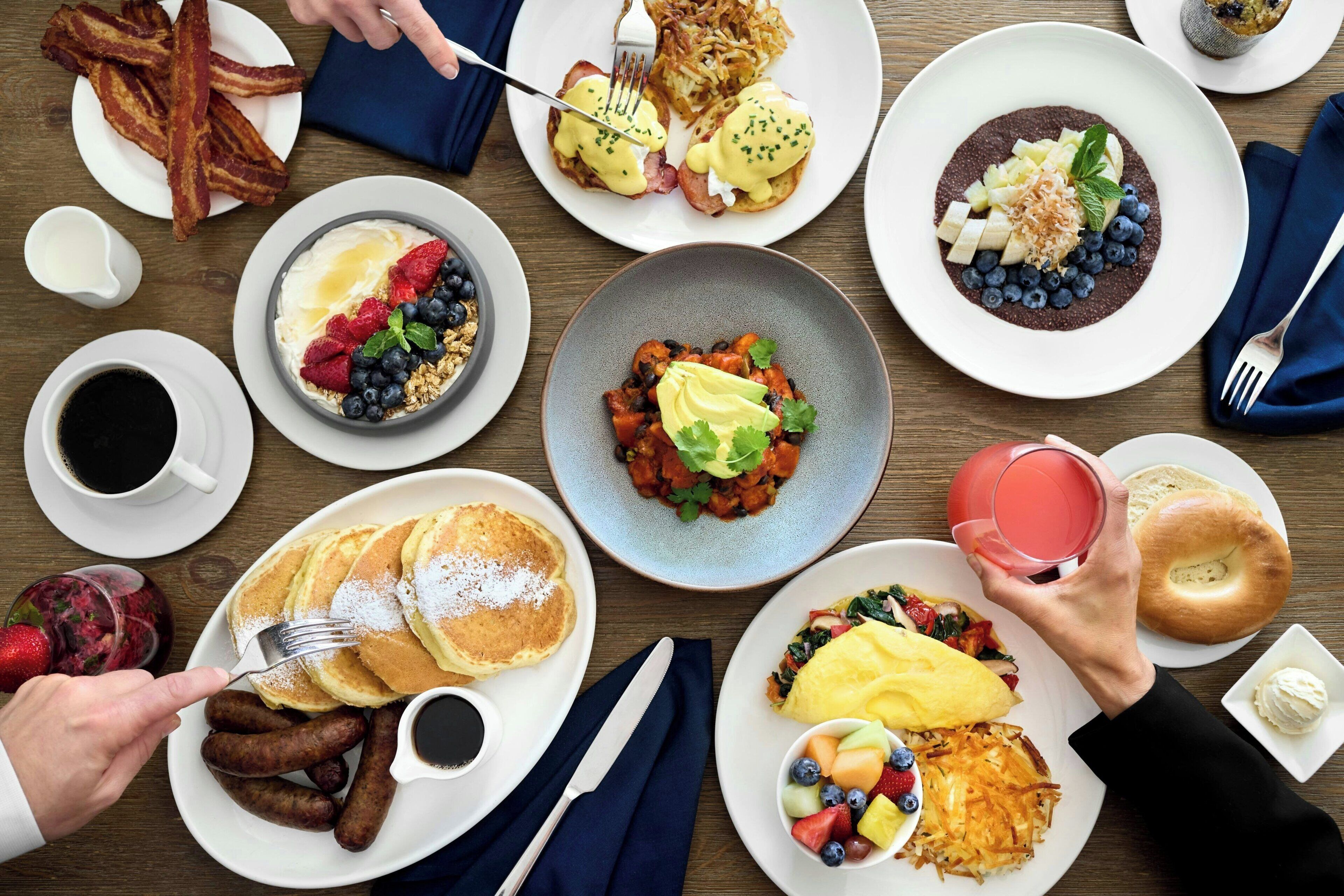 Een ontbijt met diverse gerechten, waaronder pannenkoeken, eieren, spek en een selectie fruit en groenten.