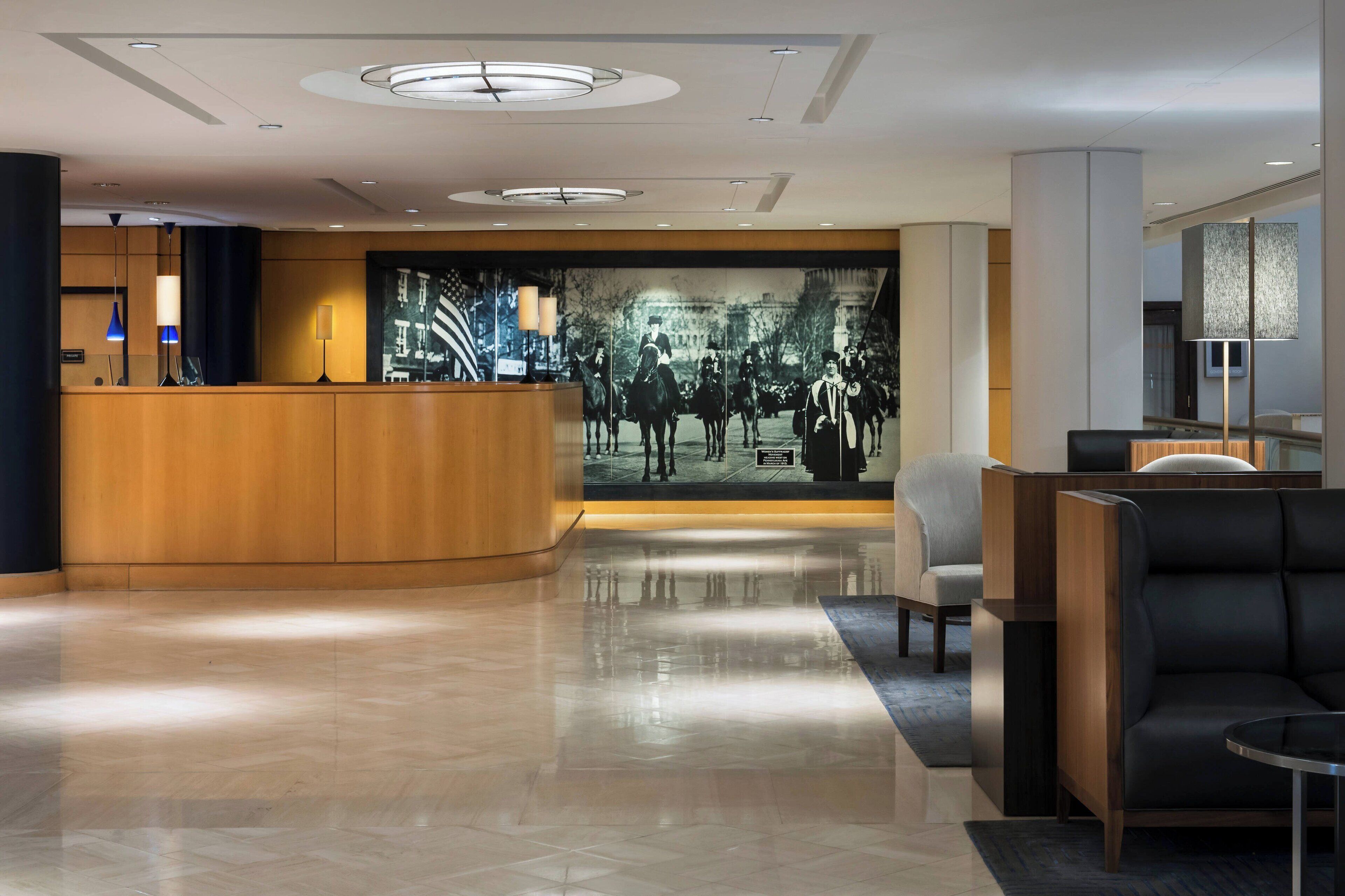 Un moderno vestíbulo de hotel con un mostrador de recepción de madera, zona de estar y un gran mural histórico.